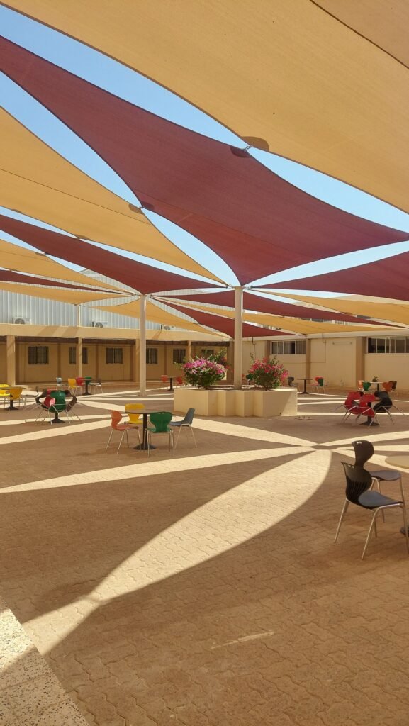 A vibrant outdoor seating area with colorful chairs and geometric sunshades casting shadows.
