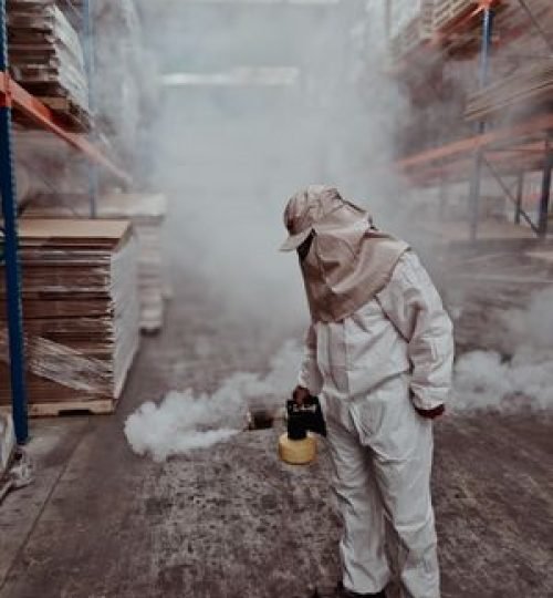 Exterminator performing fumigation in a warehouse. Safety gear and smoke management techniques in place.