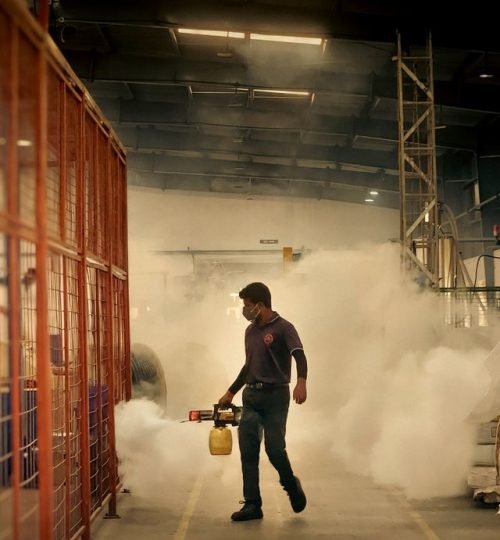 Worker fumigating inside a warehouse using a fogging machine for pest control.
